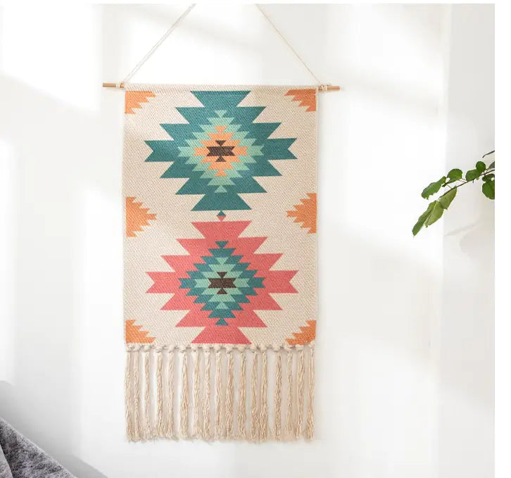 Woven wall hanging with geometric and Aztec patterns and fringes on a white wall.