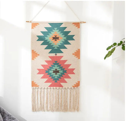 Woven wall hanging with geometric and Aztec patterns and fringes on a white wall.