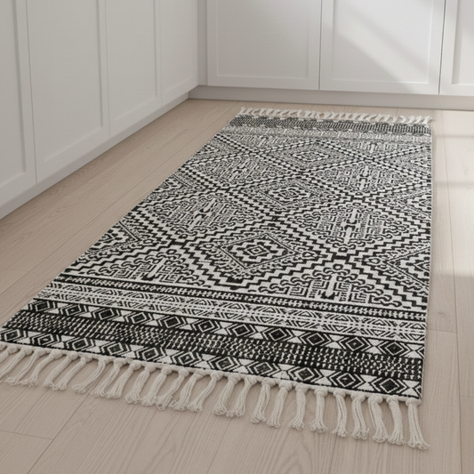 Black and white patterned rug with tassels on a wooden floor.