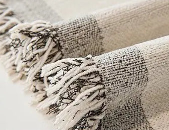 Close-up of a textured beige blanket with fringes on a neutral background
