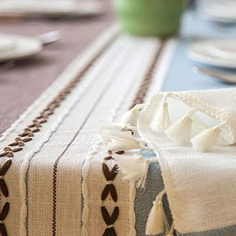Close-up of a textured tablecloth with tassels on a dining table.