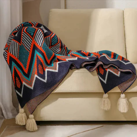 Colorful patterned blanket with tassels draped over a beige sofa.