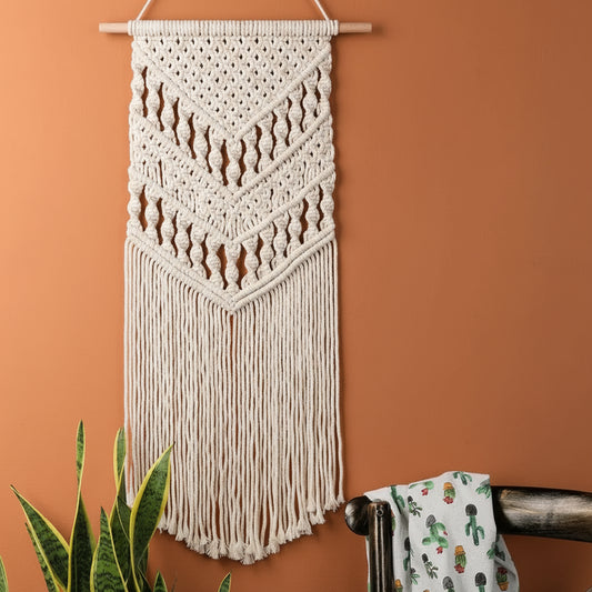 Macrame wall hanging on a white wall with a plant and chair in the foreground