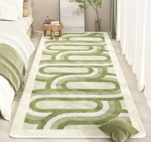 Green and white patterned rug on a light wooden floor with a bed and small table in the background.