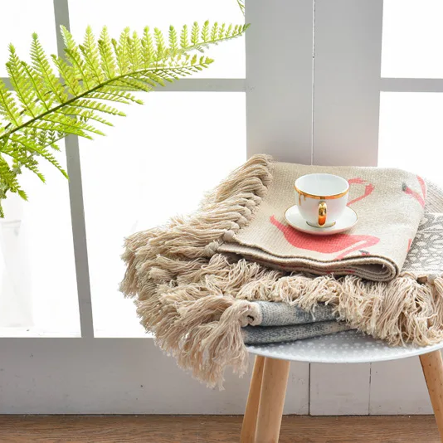 Beige blanket with a cup on a stool next to a plant