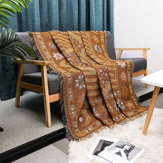 Decorative brown patterned throw blanket draped over a gray sofa in a living room setting.