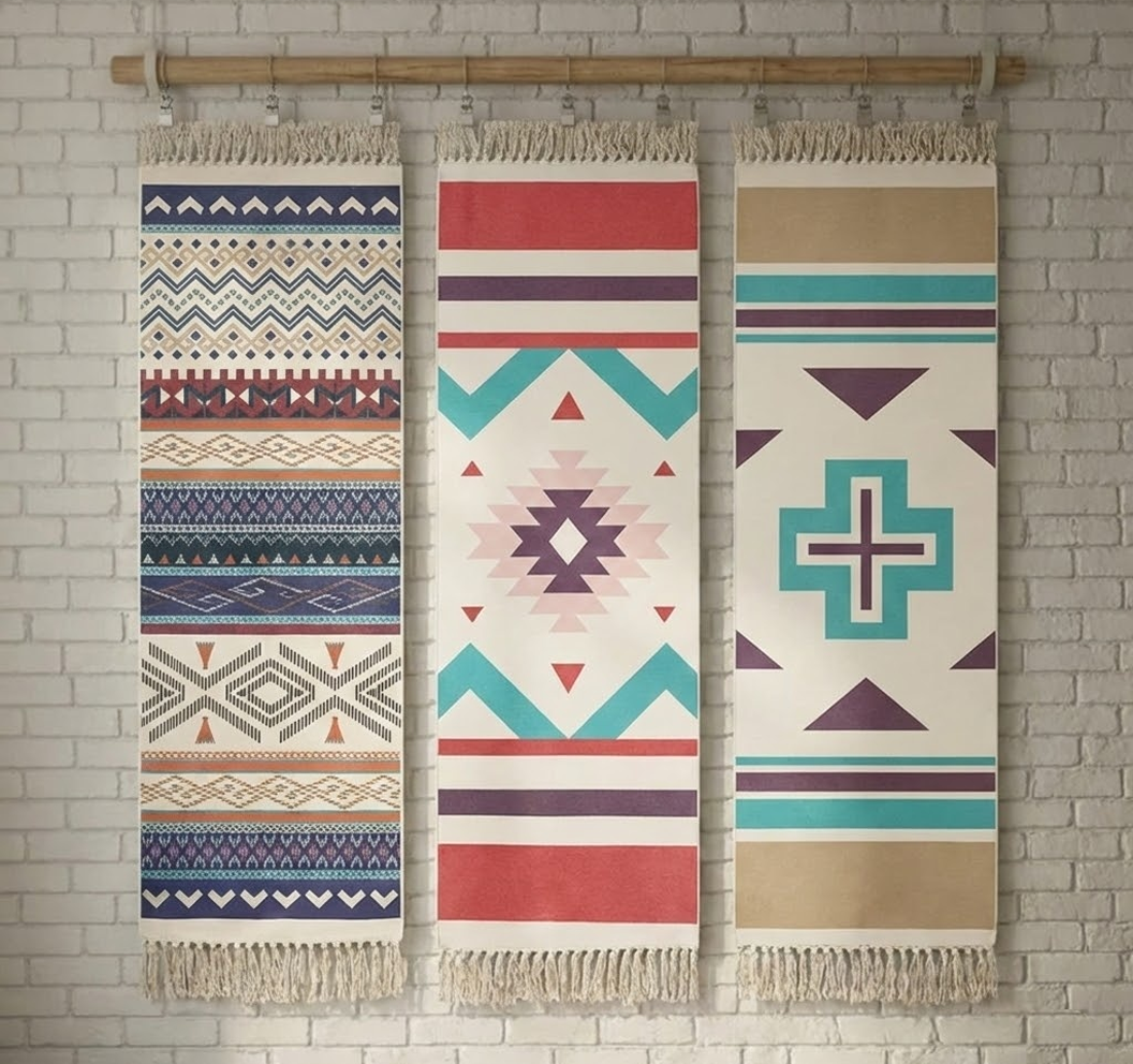 Three patterned towels hanging on a wooden rod against a brick wall.