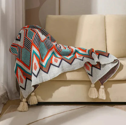 Decorative blanket with geometric pattern and tassels on a beige sofa.